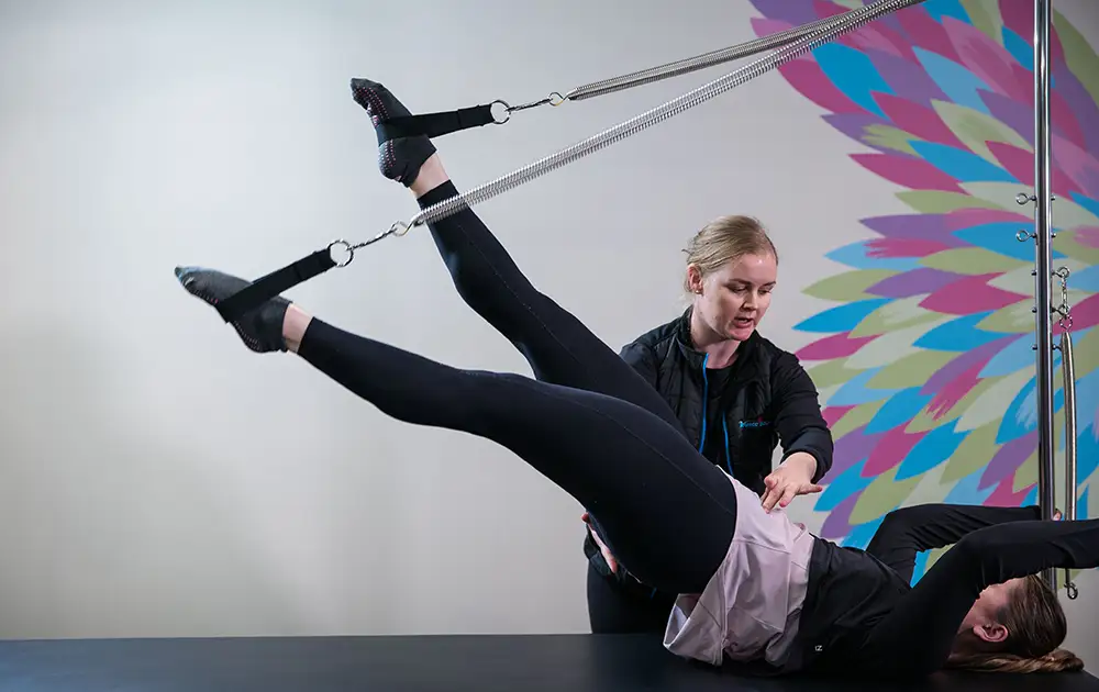 reformer Pilates teacher instructing woman through difficult physio core exercise